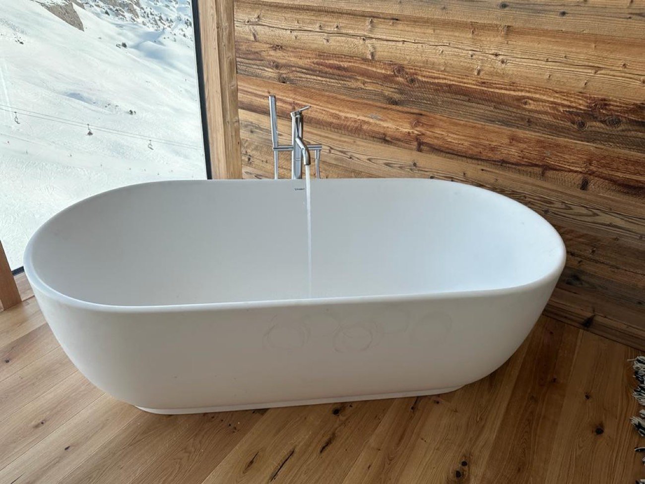 Baignoire îlot blanche avec robinetterie sur colonne dans un chalet en vieux bois
