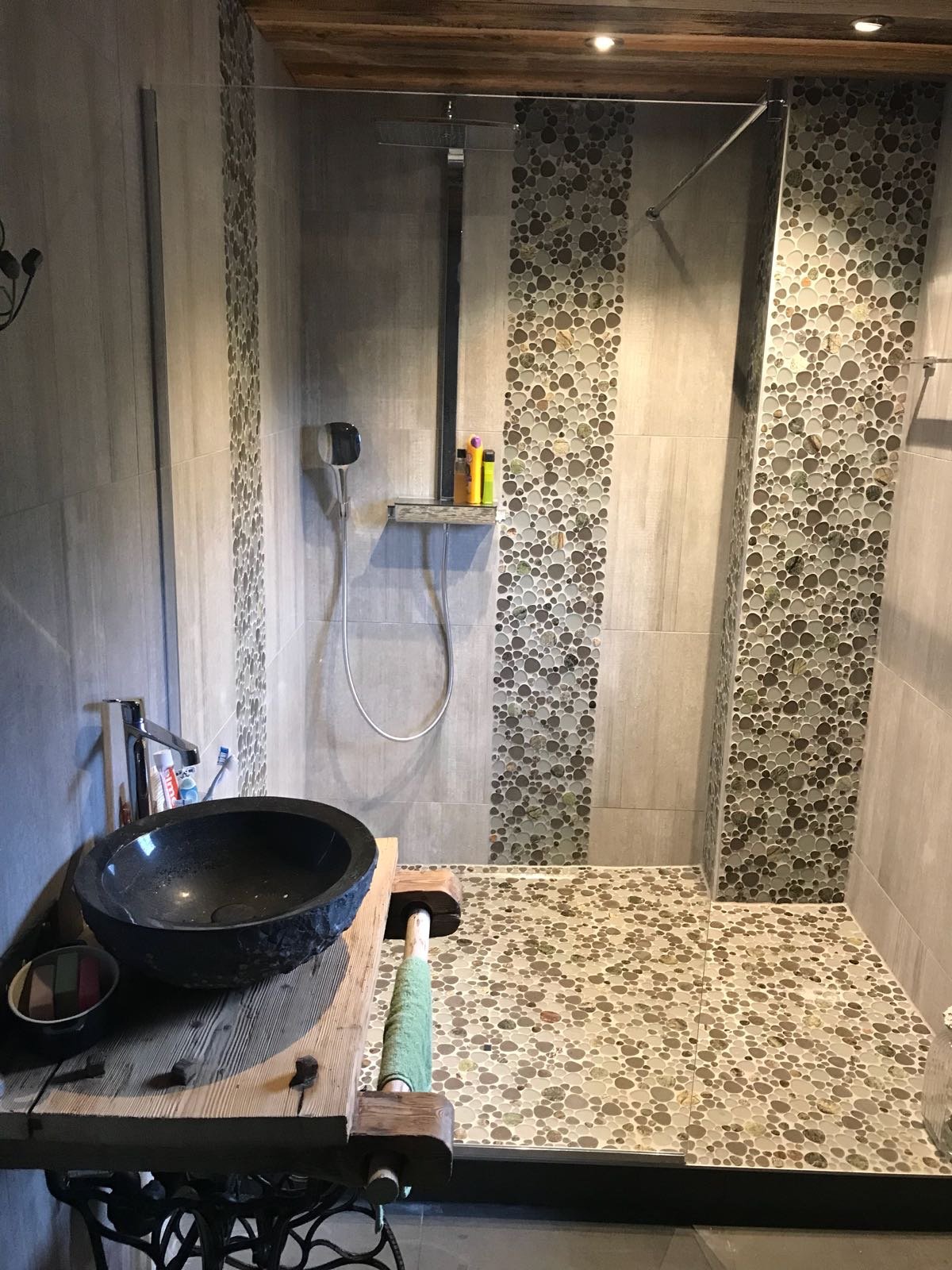 Salle de bains nature : mosaïque de galets, vasque en pierre sur plateau en vieux bois et grande douche à l'italienne