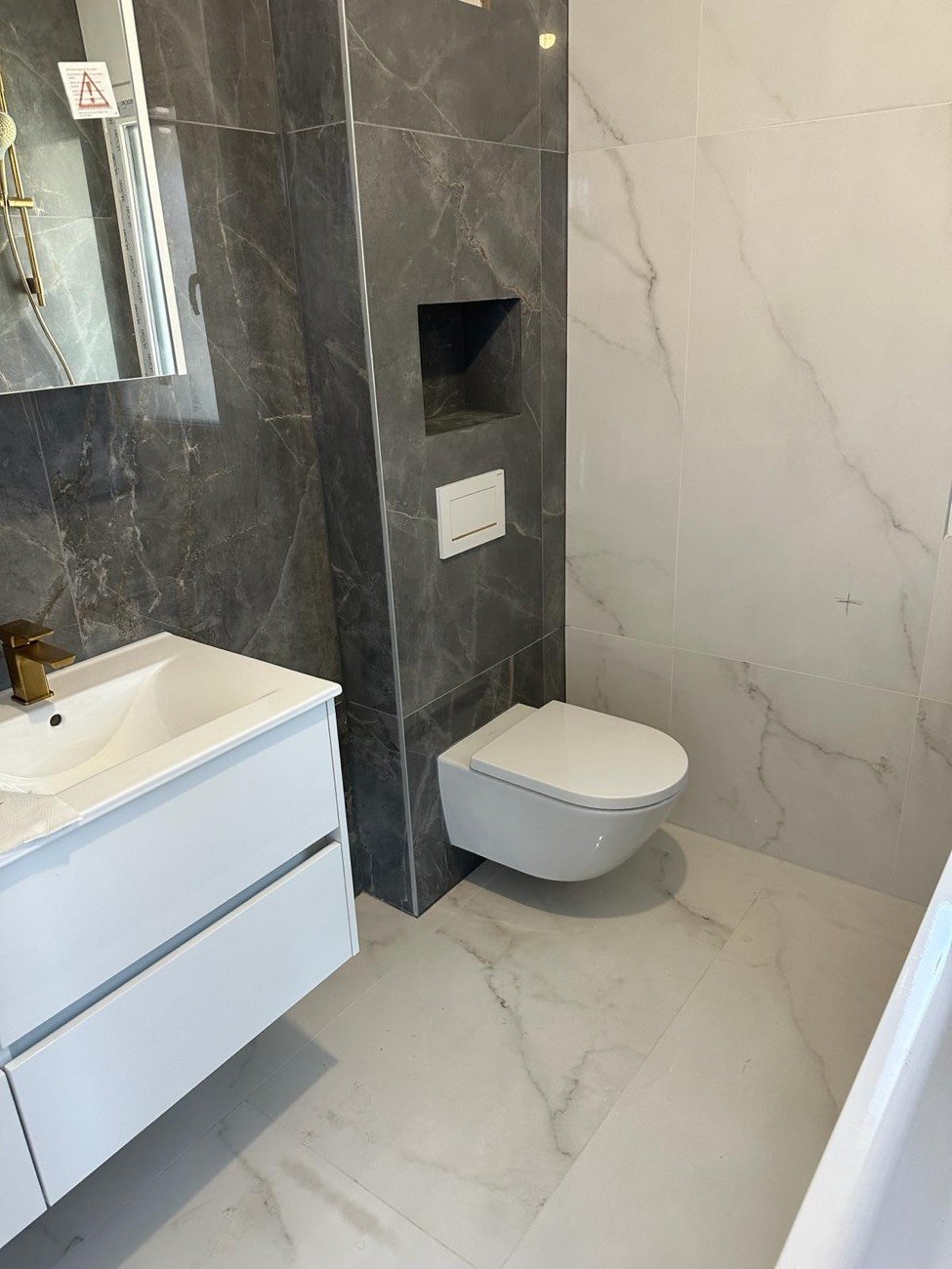 Salle de bains rénovée avec carrelage effet marbre, niche intégrée, WC suspendu et meuble vasque blanc