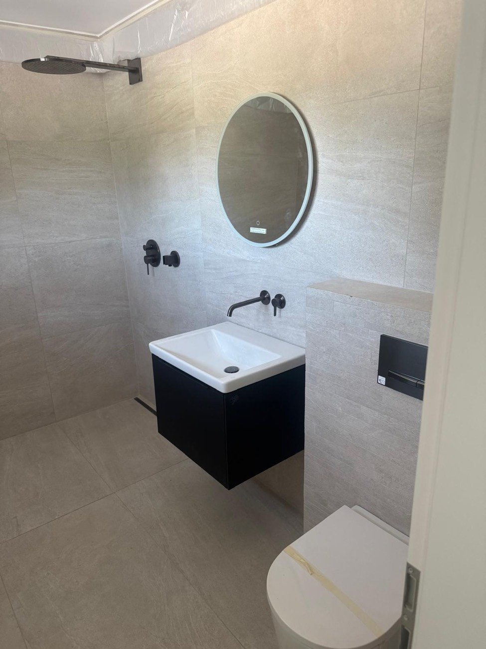 Salle de bains moderne avec meuble vasque suspendu noir, robinet mural noir et miroir rond lumineux